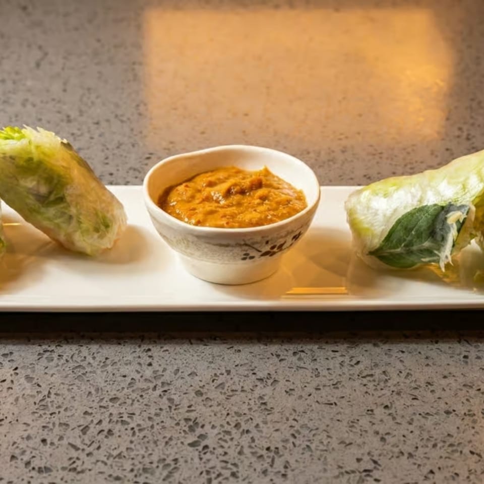 Fresh spring rolls with a side of peanut dipping sauce on a white rectangular plate.