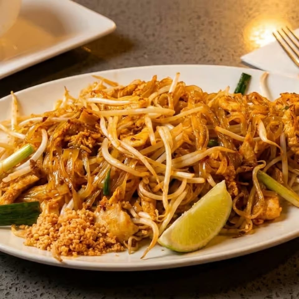 Close-up of Pad Thai noodles with bean sprouts, peanuts, and a lime wedge on a white plate.